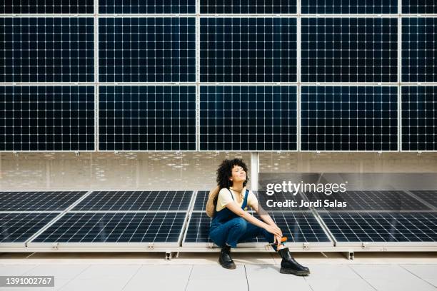 woman standing in front of a solar panel installation - painel solar imagens e fotografias de stock