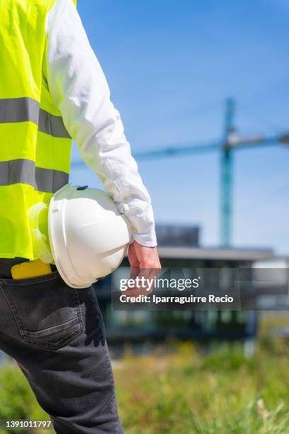 unrecognizable person from behind caucasian construction manager with helmet next to the building he is supervising and is responsible for the construction - control pants foto e immagini stock