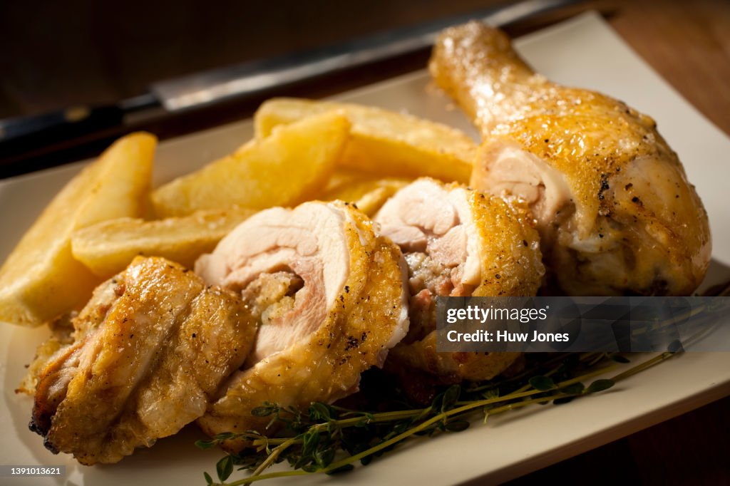 Close up roasted stuffed chicken leg on a white plate with chips