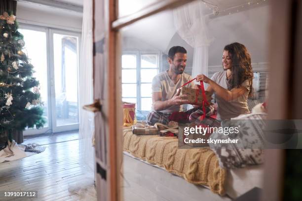 happy couple wrapping christmas presents during morning in bedroom. - serbia tradition stock pictures, royalty-free photos & images