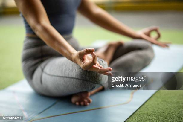 indonesian woman is meditating in a half lotus position at a gym - yoga stock-fotos und bilder