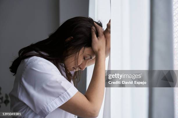 exhausted and stressed female doctor leaning on a window while working from home. - woman collapsing stock pictures, royalty-free photos & images