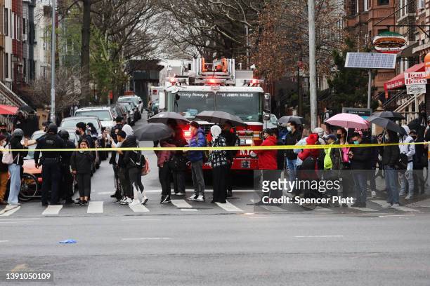 Onlookers watch as police and emergency responders gather at the site of a reported shooting of multiple people outside of the 36 St subway station...