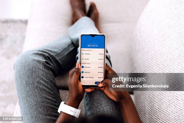 overhead view of young black woman managing online banking with smartphone sitting on the sofa at home. - online banking app stock pictures, royalty-free photos & images