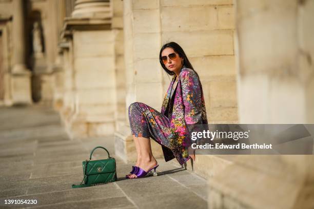 Gabriella Berdugo wears brown sunglasses, a silver with diamond pendant necklace, a gray V-neck cropped t-shirt, a black with embroidered gold and...