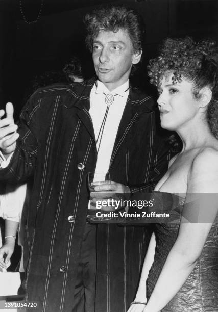 American singer Barry Manilow, wearing a jacket with white vertical stripes, a white shirt and a bolo tie, with American actress and singer...