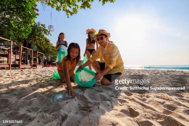 happy asian family clean up the beach by pick up the trash into the garbage bag. volunteer and environmental conservation concept. - father and children volunteering stock pictures, royalty-free photos & images