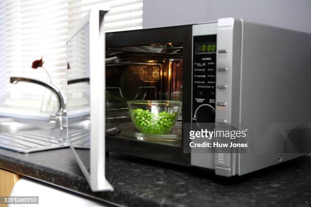 a glass bowl of frozen peas inside a microwave in a home kitchen - peas stock pictures, royalty-free photos & images