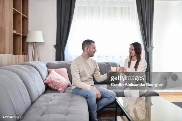smiling couple sitting and enjoying drinks in living room after work - drunk wife at party stockfoto's en -beelden
