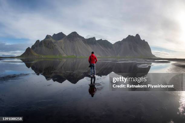 a man with gorgeous black sand dunes on stokksnes cape in iceland. location: stokksnes cape, vestrahorn (batman mount), iceland, europe - black sand iceland stock-fotos und bilder