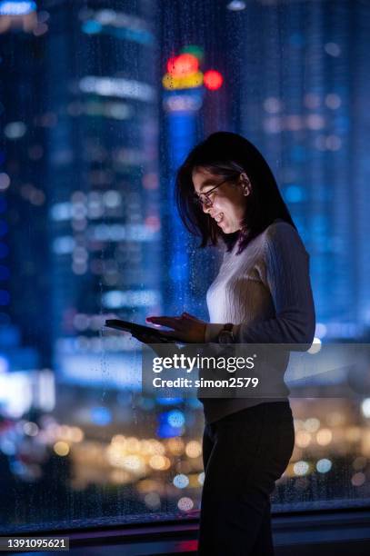 reading the latest in business news online. an asian business woman working at night online on a digital tablet - singapore night stock pictures, royalty-free photos & images