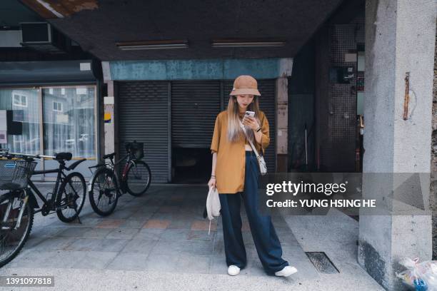 in asia, a young taiwanese waits for friends on the street. - phone street style stock pictures, royalty-free photos & images