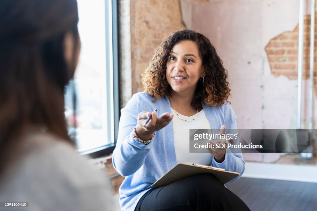 Meeting one-on-one, female therapist gestures toward unrecognizable woman
