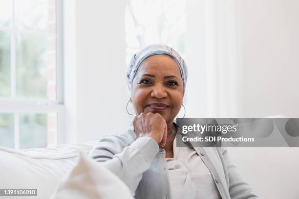 serene female senior adult cancer patient smiles for camera - headscarf home stockfoto's en -beelden