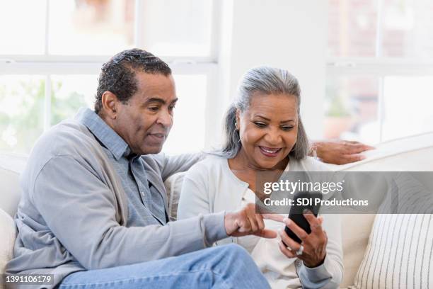 husband helps point something out on his wife's phone - couple pointing imagens e fotografias de stock