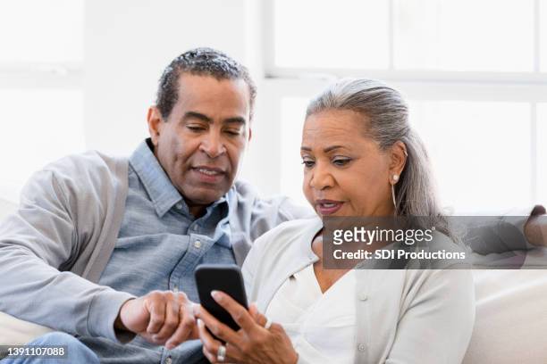senior husband helps wife with mobile apps on phone - african american man helping elderly bildbanksfoton och bilder