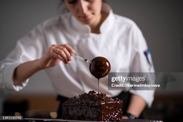 une boulangère versant de la sauce au chocolat sur un gâteau - pâtissier photos et images de collection