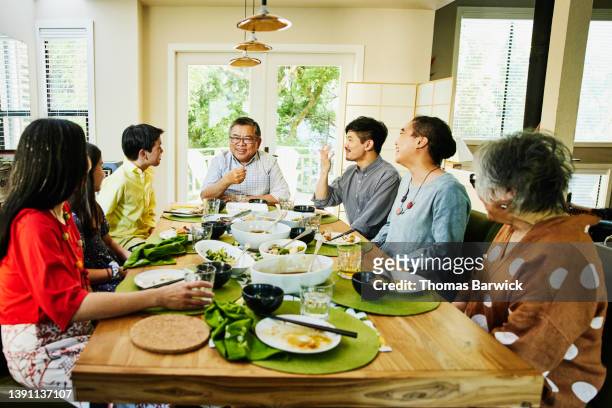 wide shot of smiling and laughing multigenerational family in discussion during dinner party - girl sitting on boys face fotografías e imágenes de stock