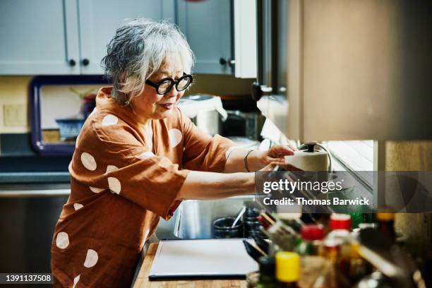 medium wide shot of senior woman cleaning up in kitchen after dinner with family - true peoples celebration day one stock pictures, royalty-free photos & images