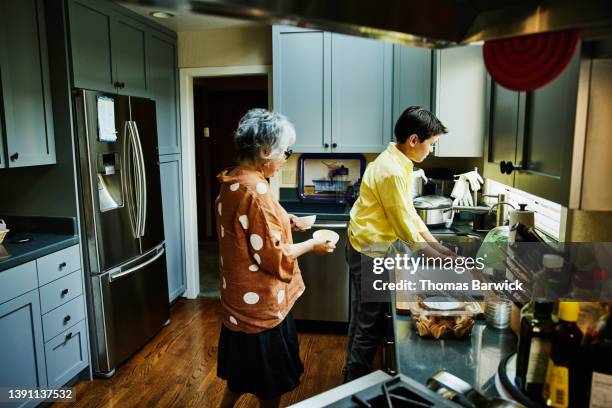 wide shot of grandson helping grandmother with dishes in kitchen after family dinner party - cleaning after party stock pictures, royalty-free photos & images