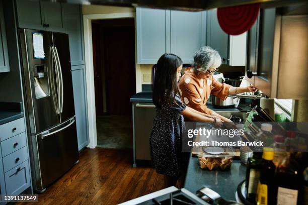 wide shot of granddaughter helping grandmother with dishes in kitchen after family dinner party - children housework stock pictures, royalty-free photos & images