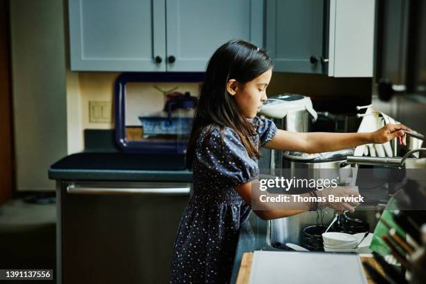 medium wide shot of girl doing dishes in kitchen after family dinner party - cleaning up after party stock-fotos und bilder