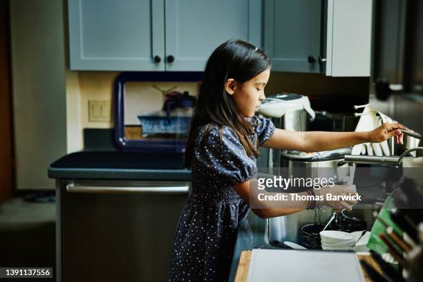 medium wide shot of girl doing dishes in kitchen after family dinner party - responsibility stock pictures, royalty-free photos & images