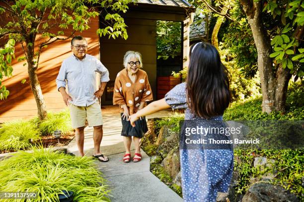 wide shot of granddaughter running to greet grandparents in front of home on summer evening - couple short hair stock pictures, royalty-free photos & images