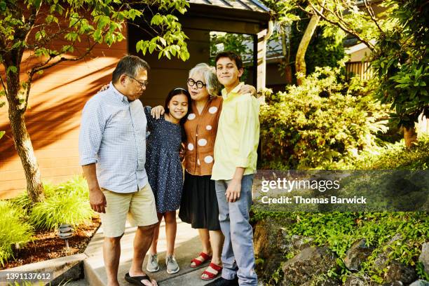 wide shot portrait of grandparents hugging grandchildren in front of home on summer evening - family of four in front of house stock pictures, royalty-free photos & images