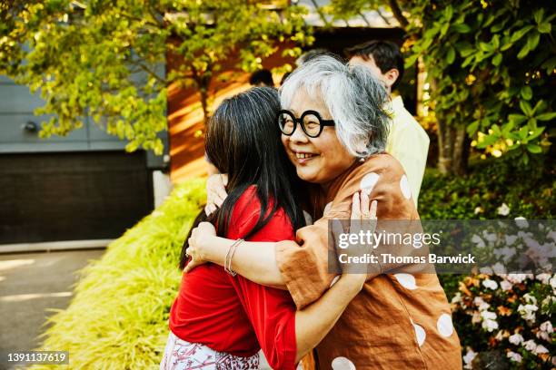 medium shot of smiling grandmother hugging daughter before family party on summer evening - chinese ethnicity stock pictures, royalty-free photos & images