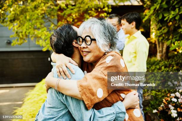 medium shot of smiling grandmother hugging family member before family party on summer evening - oma feiert stock-fotos und bilder