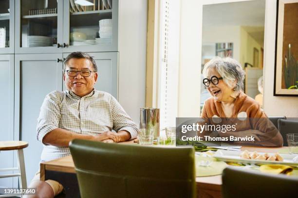 medium wide shot of smiling and laughing senior couple relaxing at dining room table after dinner party - table after party stock pictures, royalty-free photos & images