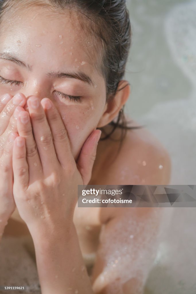 Close up face Asian woman relaxing while taking a shower in bath tub