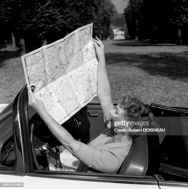 Actrice Paulette Dubost regardant une carte routière dans une voiture décapotable pour une publicité automobile, 1959.