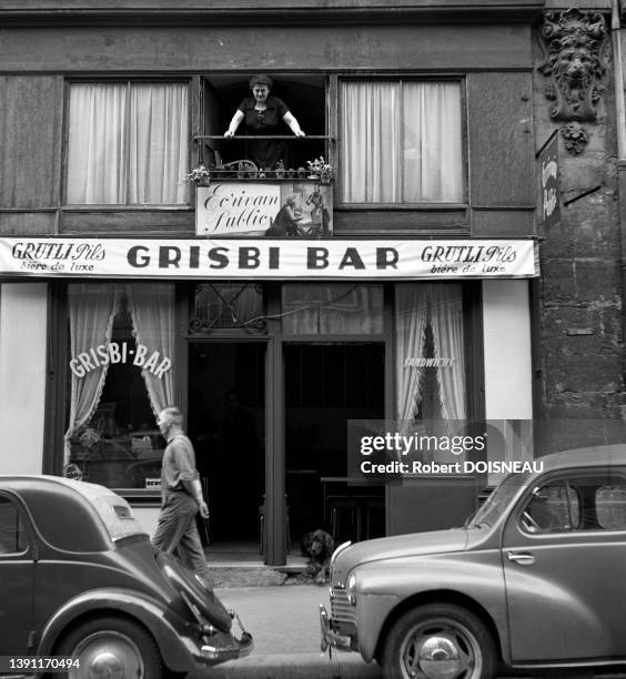 Vitrine du bar à bières de luxe le "Grisbi Bar" et femme à son balcon juste au dessus à Paris en juillet 1955.