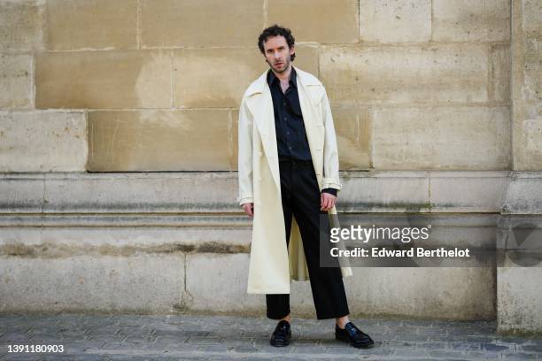 Lukas Osiecki wears a black shirt, a white latte long coat, black large suit pants, black shiny leather loafers from Prada, during a street style...