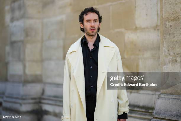 Lukas Osiecki wears a black shirt, a white latte long coat, black large suit pants, during a street style fashion photo session, on April 11, 2022 in...
