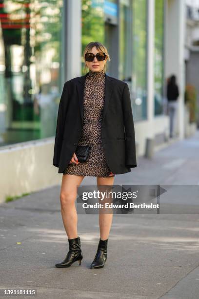 Emy Venturini wears black sunglasses, gold fringed chain pendant earrings, a brown / black leopard print pattern turtleneck tube short dress, a black...