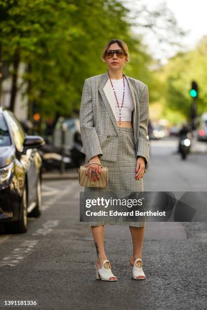 Emy Venturini wears brown sunglasses, silver earrings, a burgundy pearls long necklace, a white ribbed / cropped t-shirt, a gray and white checkered...