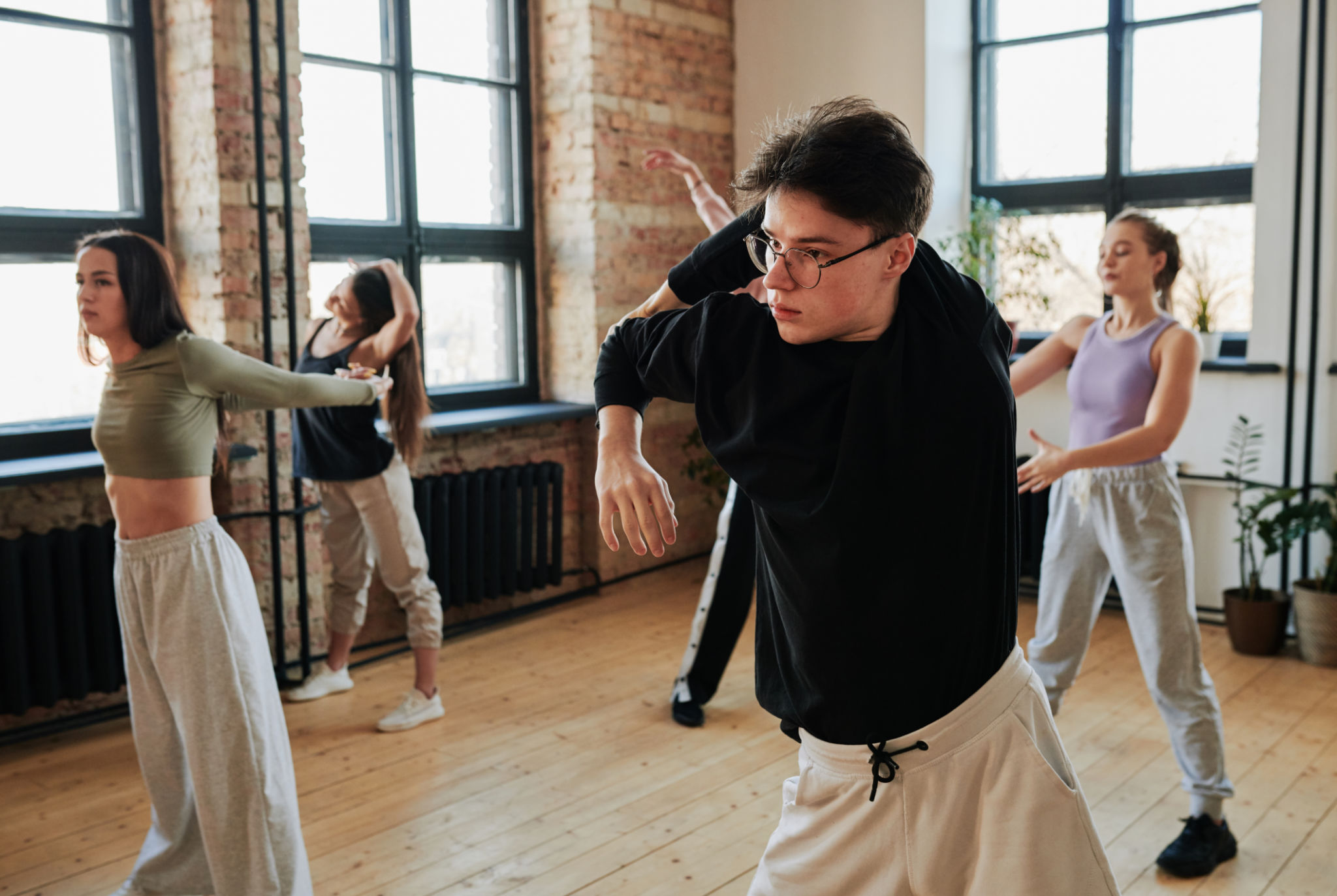 Flexible teenage guy in black sweatshirt and white pants training in dance hall Flexible teenage guy in black sweatshirt and white pants training in dance hall