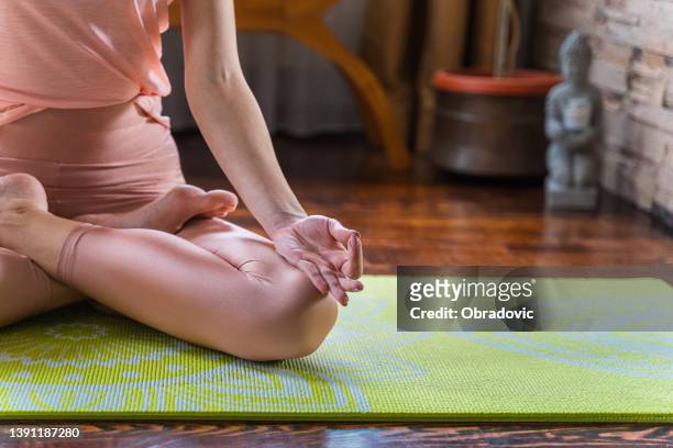 scatto ritagliato di una donna irriconoscibile seduta su un tappetino da yoga e che medita da sola nella sua casa - lotus foto e immagini stock