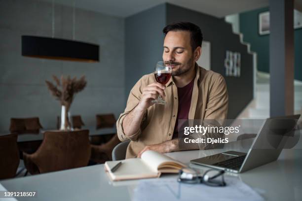 happy young man enjoying wine while taking a break from work at home. - wine tasting online stock pictures, royalty-free photos & images