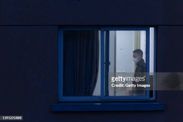 Man with a mask is seen through a window at his home in a residential area on April 13, 2022 in Shanghai, China. Some 25 million people in Shanghai...