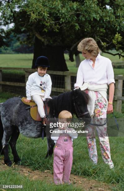 British Royal Prince William riding Smokey the pony as his mother, Diana, Princess of Wales , wearing a white shirt and floral pattern trousers, and...