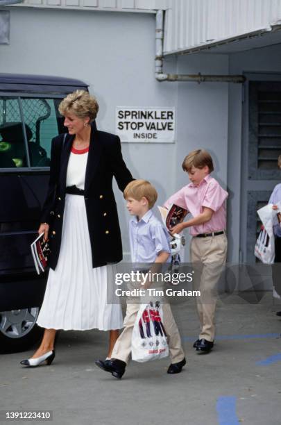 British Royals Diana, Prince of Wales , wearing a black blazer with brass buttons over a white dress with a red collar and a black belt, and her sons...