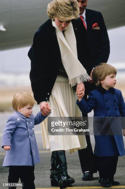 British Royal Diana, Princess of Wales , wearing a grey, black and white sweater under a black jacket with a cream scarf and cream skirt, holding the...