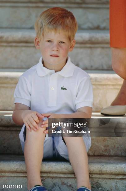 British Royal Prince Harry, wearing a white Lacoste polo shirt and pale blue shorts sitting on the steps of the Palace of Marivent in Palma de...