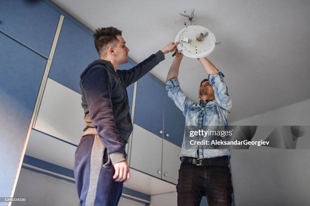Teamwork By Male Friends Repairing And Setting Up Ceiling Light