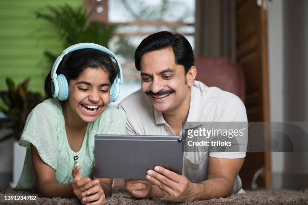 father and daughter listening music and watching video on digital tablet - indian music 個照片及圖片檔
