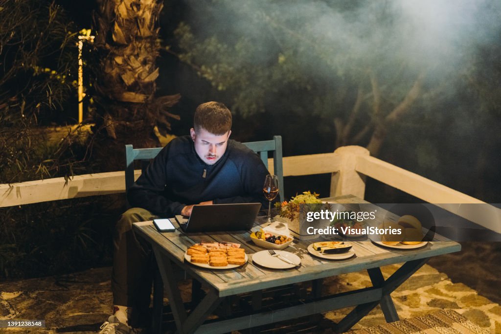 Male working by laptop during barbecue picnic with burgers at the home terrace